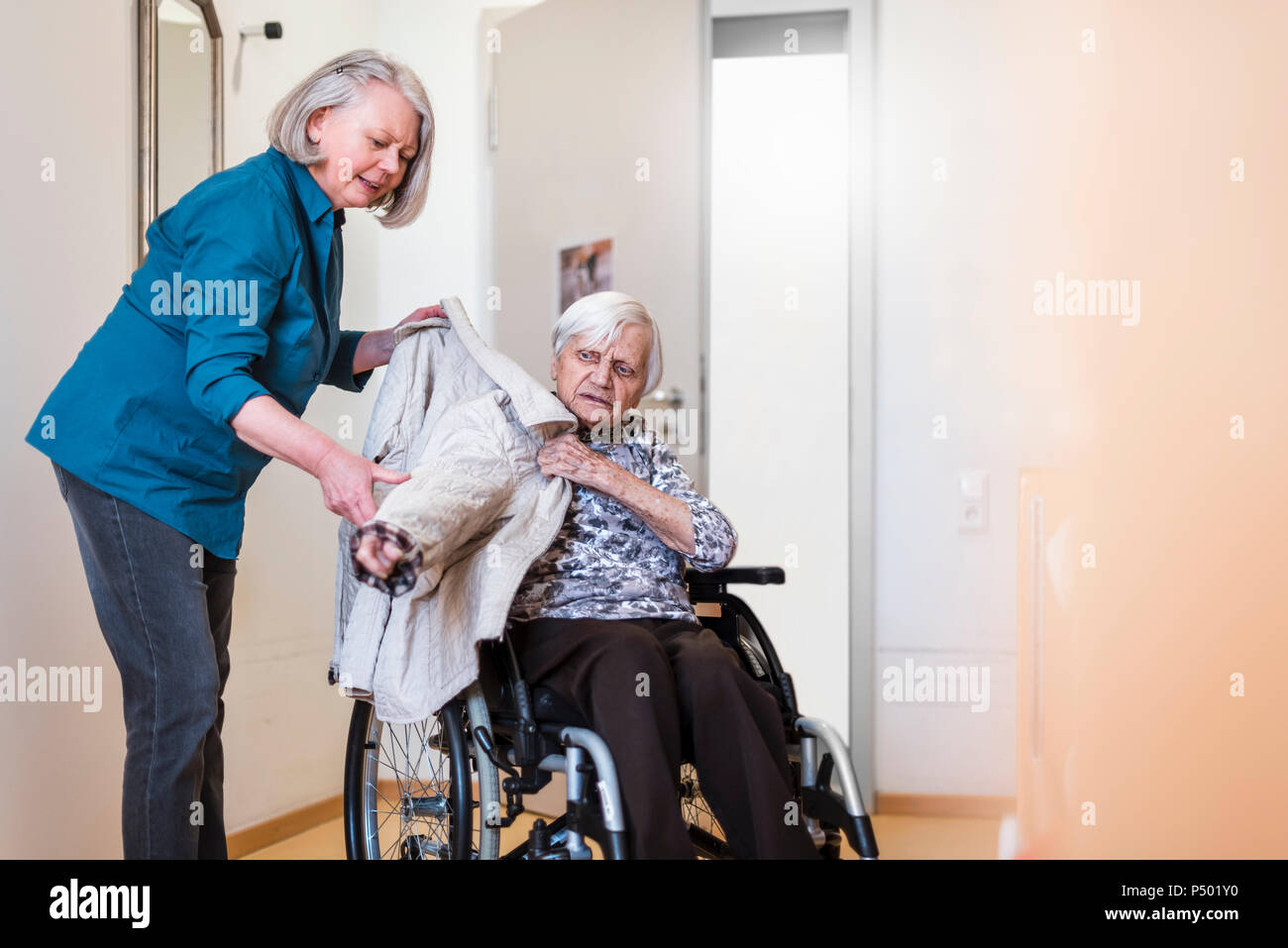 Frau kümmert sich um alte Frau im Rollstuhl setzen ihre Jacke auf Stockfoto