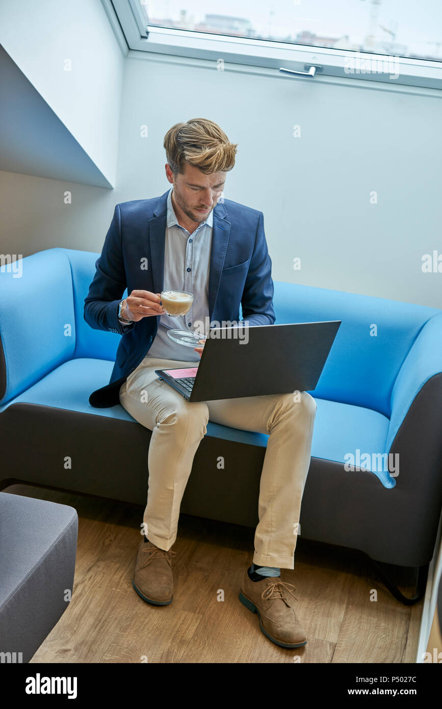 Unternehmer sitzen auf der Couch mit Tasse Kaffee auf Laptop Stockfoto