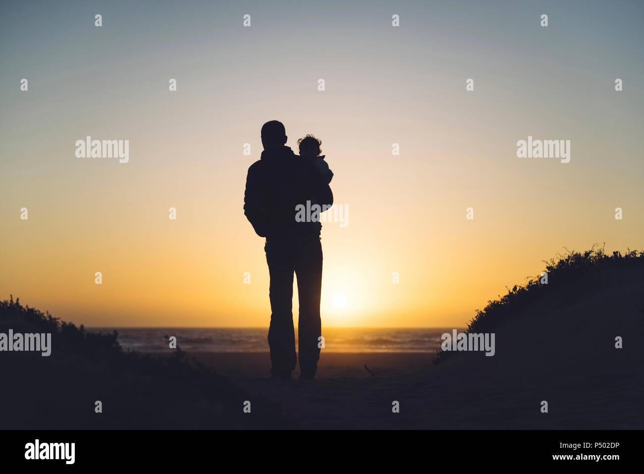 USA, Kalifornien, Morro Bay, Silhouetten von Vater und Baby Sonnenuntergang am Strand Stockfoto