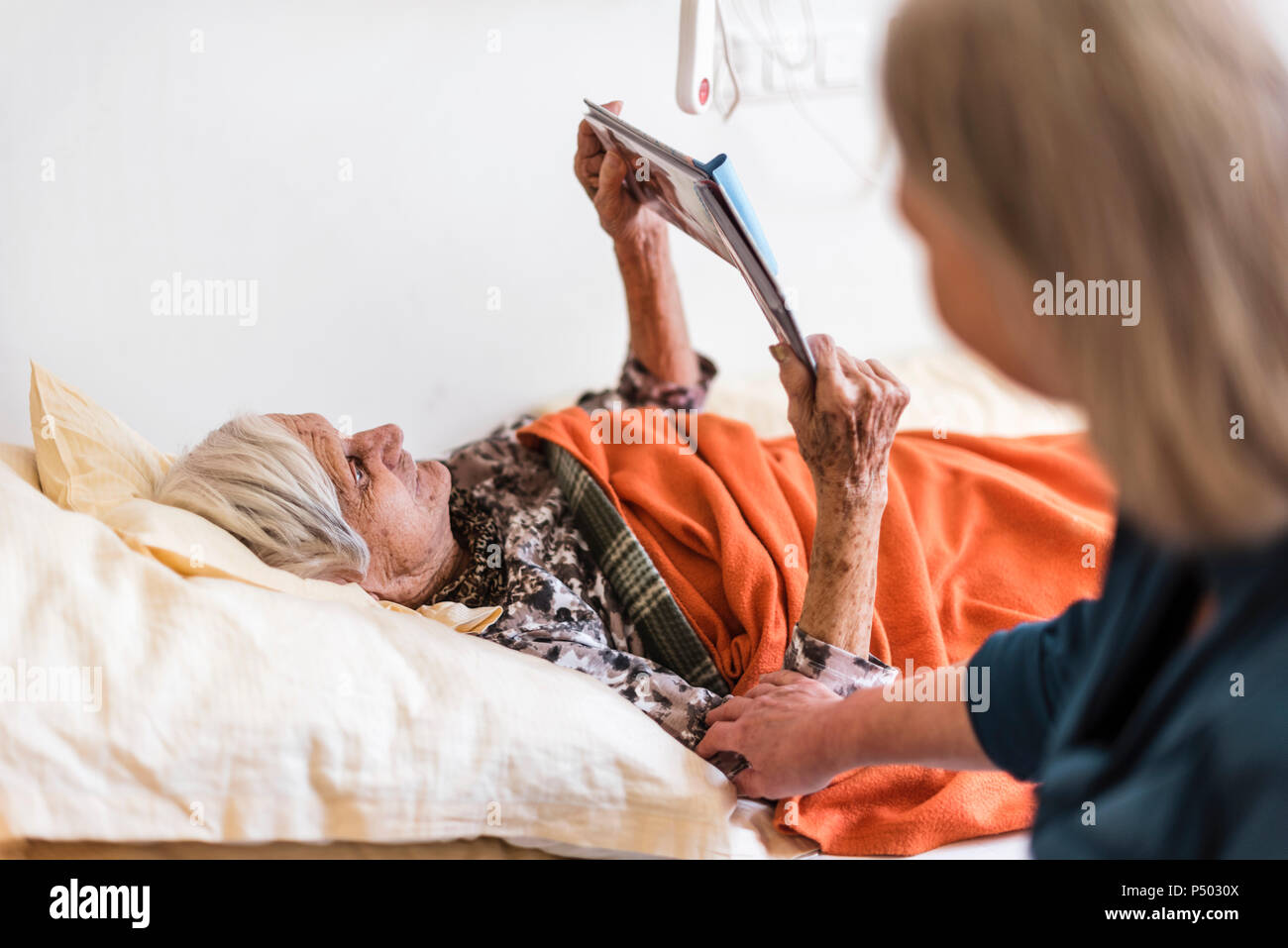 Frau kümmert sich um alte Frau im Bett lesen Buch liegen Stockfoto