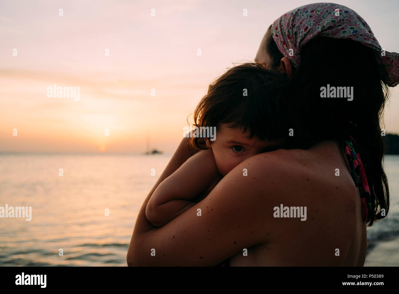 Mutter, die kleine Tochter auf dem Arm vor dem Meer Sonnenuntergang beobachten Stockfoto