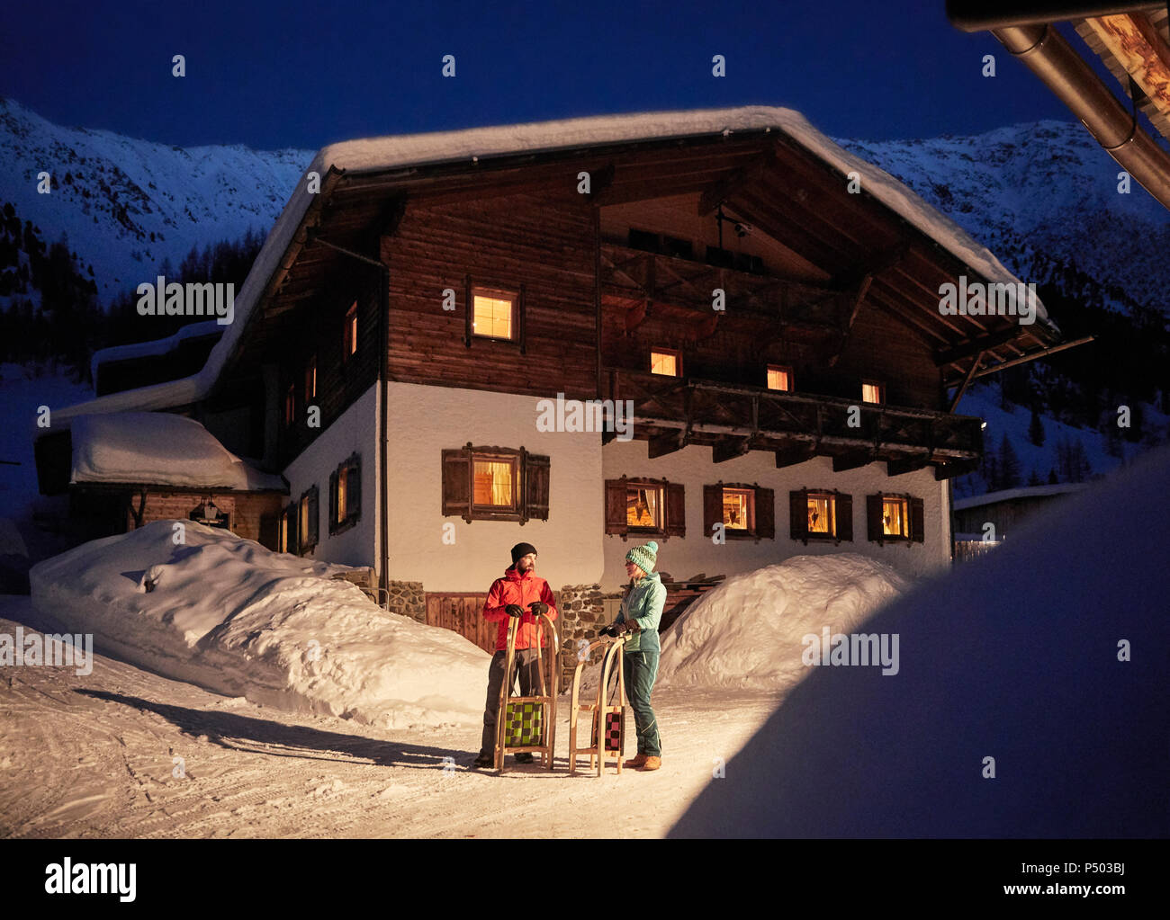 Paar mit Schlitten in der verschneiten Landschaft mit rustikalen Haus in der Nacht Stockfoto