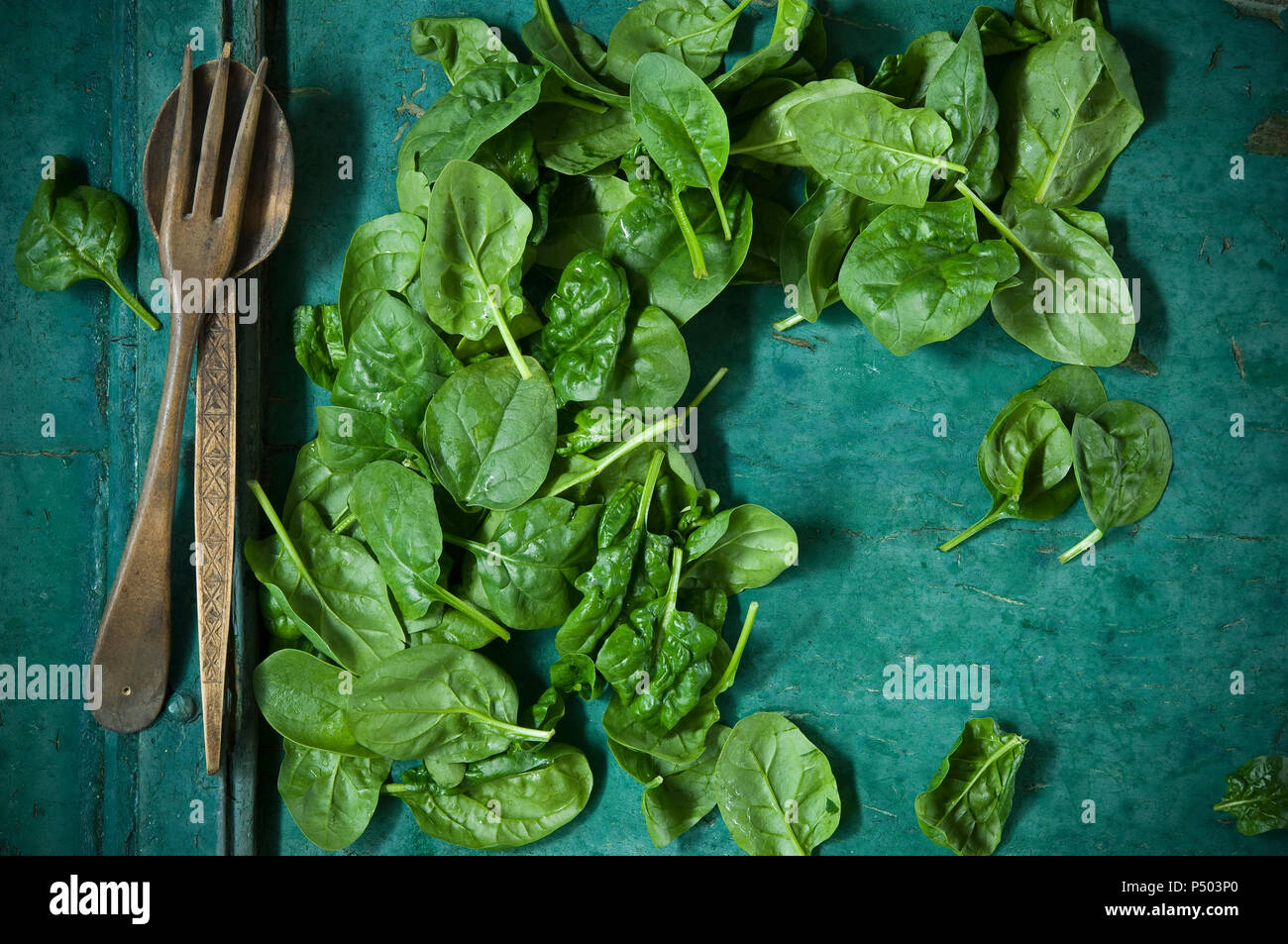 Spinatblätter und Salat Besteck auf grünem Hintergrund Stockfoto