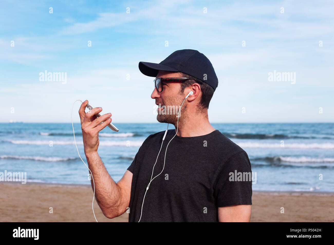 Mann mit Smartphone und Ohrhörer am Strand Stockfoto