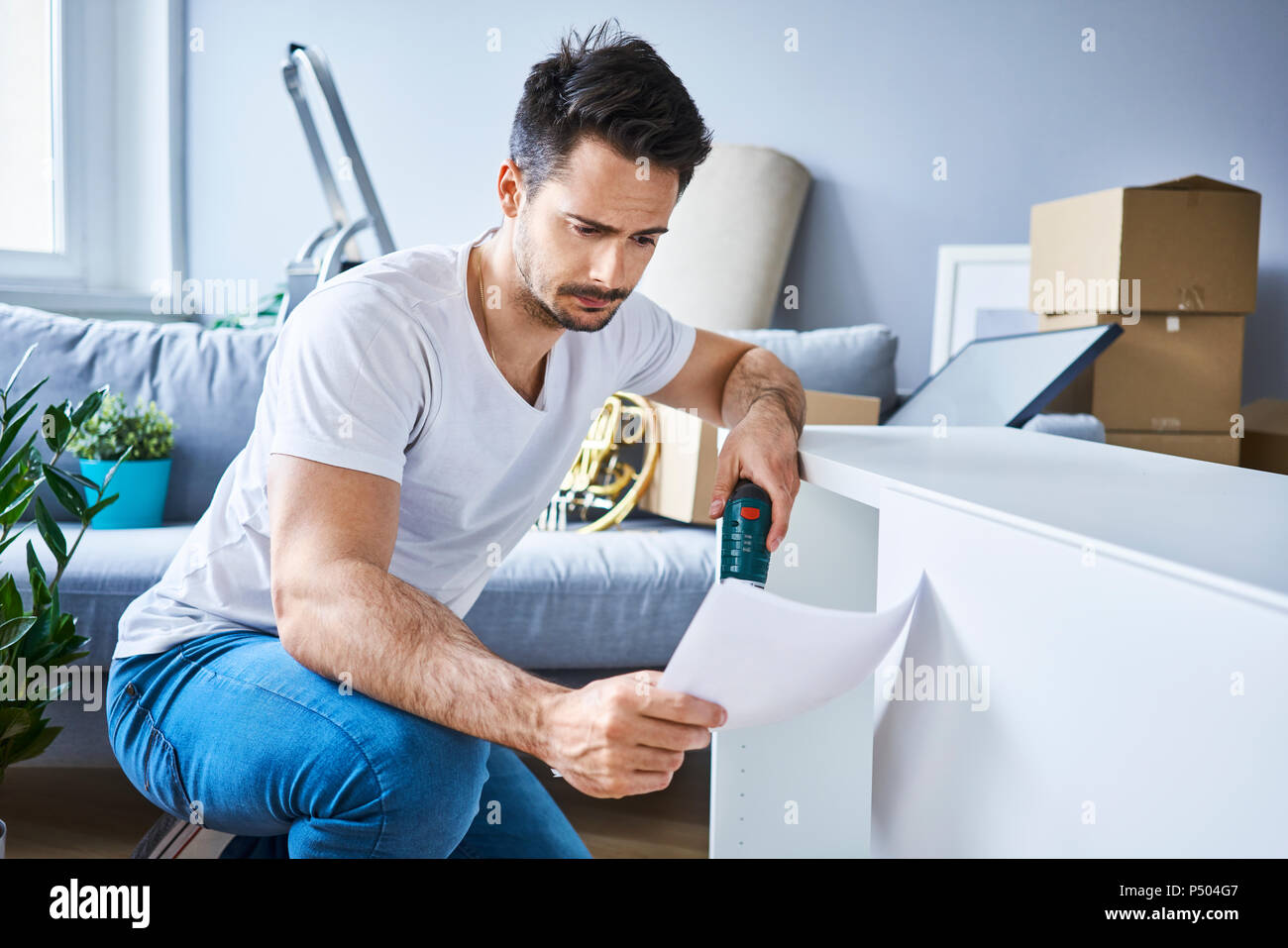 Mann Lesen der Anweisungen während der Montage Möbel in der neuen Wohnung Stockfoto