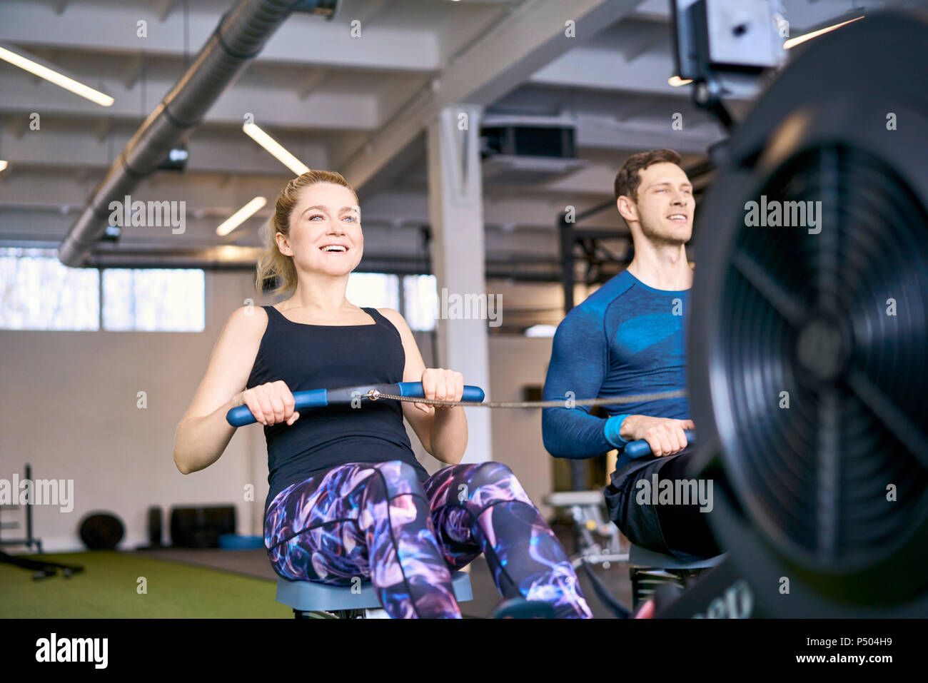 Mann und Frau im Fitnessstudio trainieren zusammen auf Rudergeräte Stockfoto