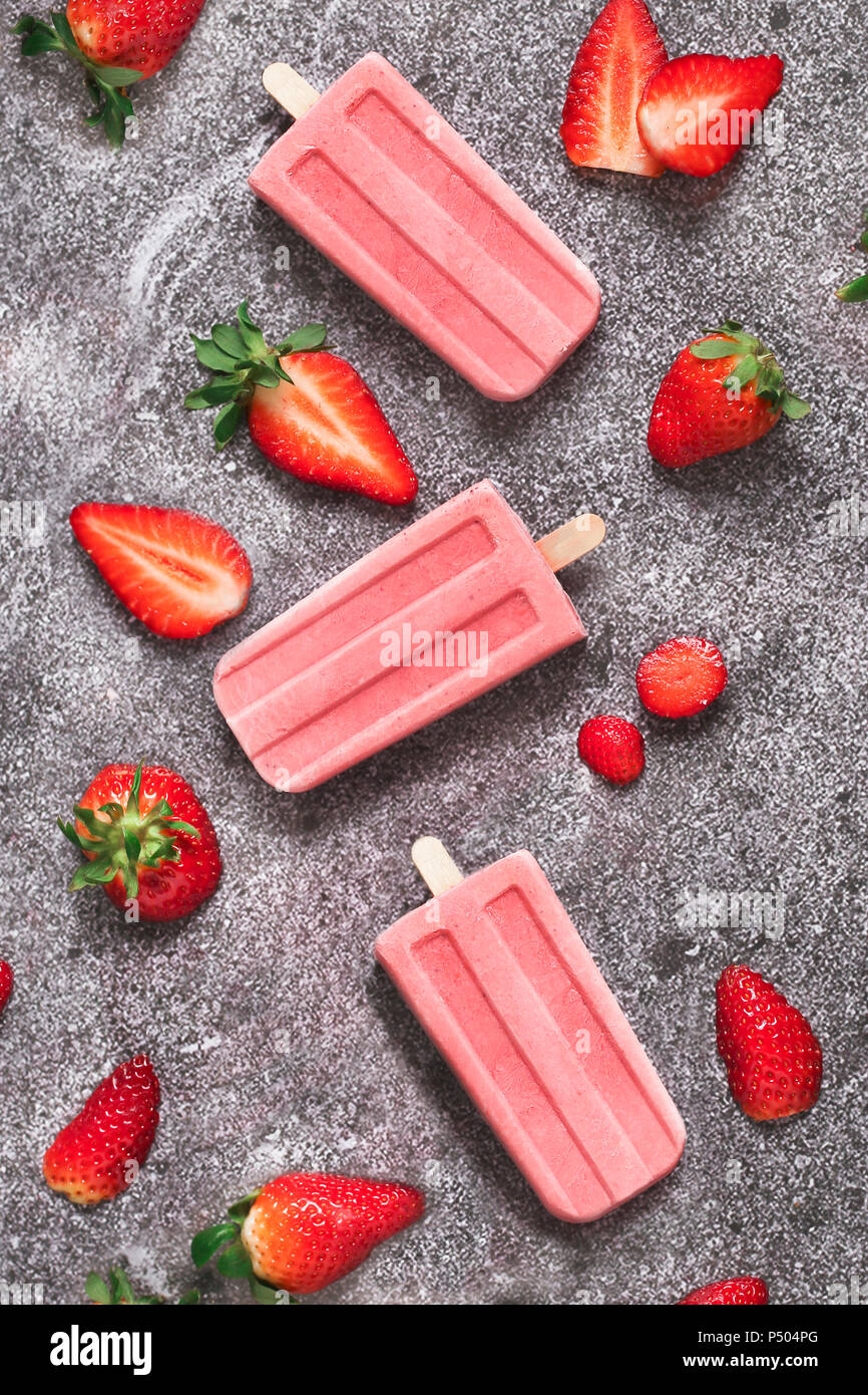 Drei selbstgemachte Erdbeer Eis am Stiel und Erdbeeren auf Marmor Stockfoto