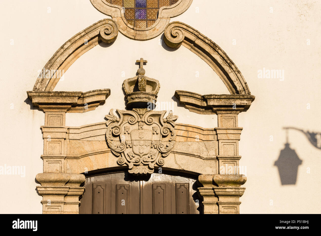 Tür mit geschwungenen Giebel und Stein Wappen oben, und Schatten der Stadt Licht an der Wand. Igreja da Misericordia Kirche, Trancoso, Portugal. Stockfoto