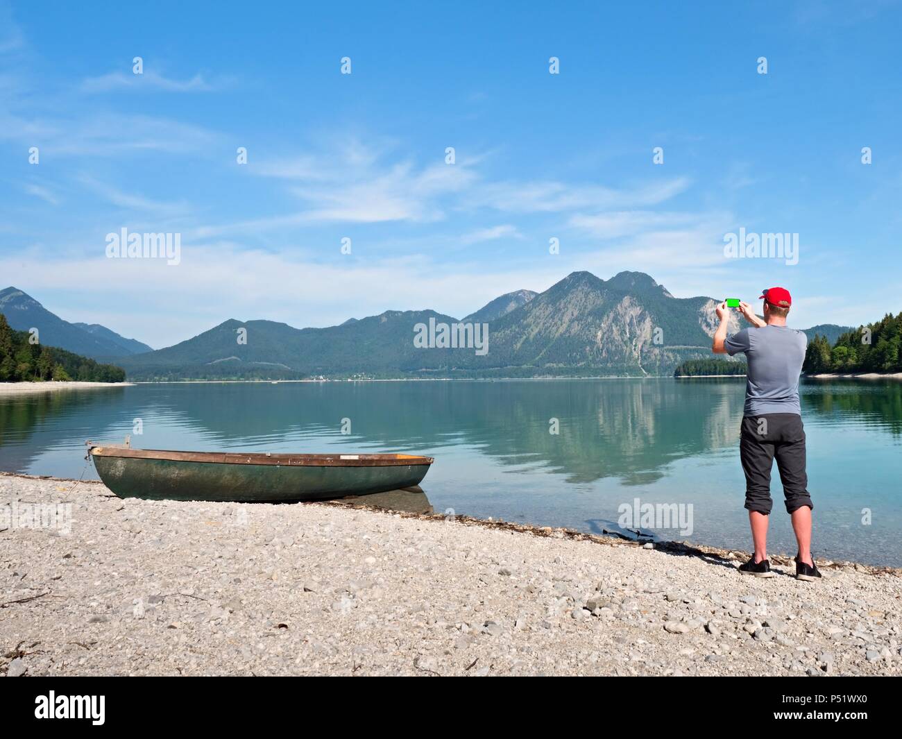 Fotograf mit Auge am Sucher ist unter Foto von See mit Alpen Berge im Hintergrund. Künstler arbeitet. Stockfoto