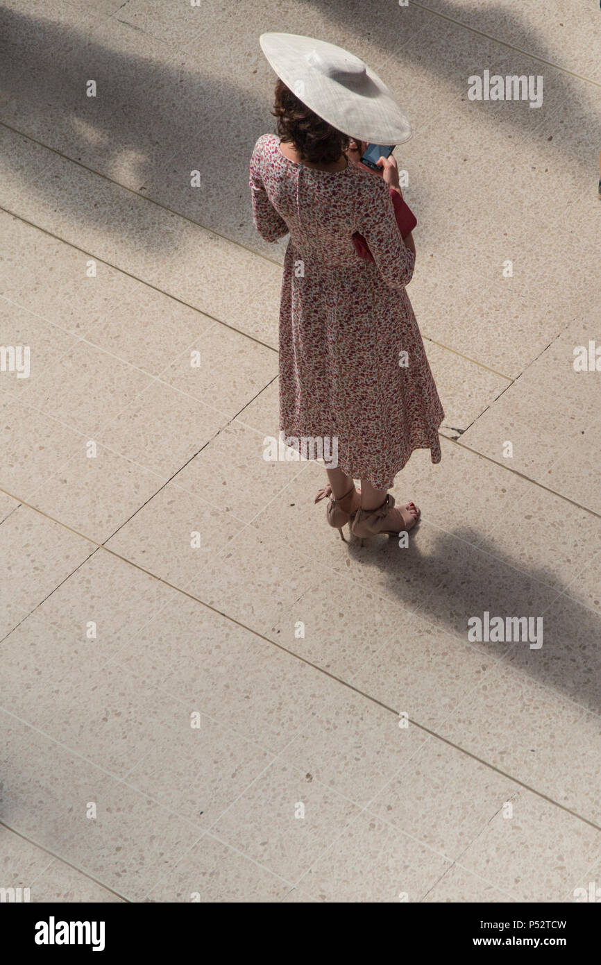 Eine geheimnisvolle, schöne Frau steht allein auf einem Bahnsteig, auf Ihr Telefon suchen, tragen ein hübsches Kleid und einem Hut mit breiter Krempe, glamourösen Stockfoto