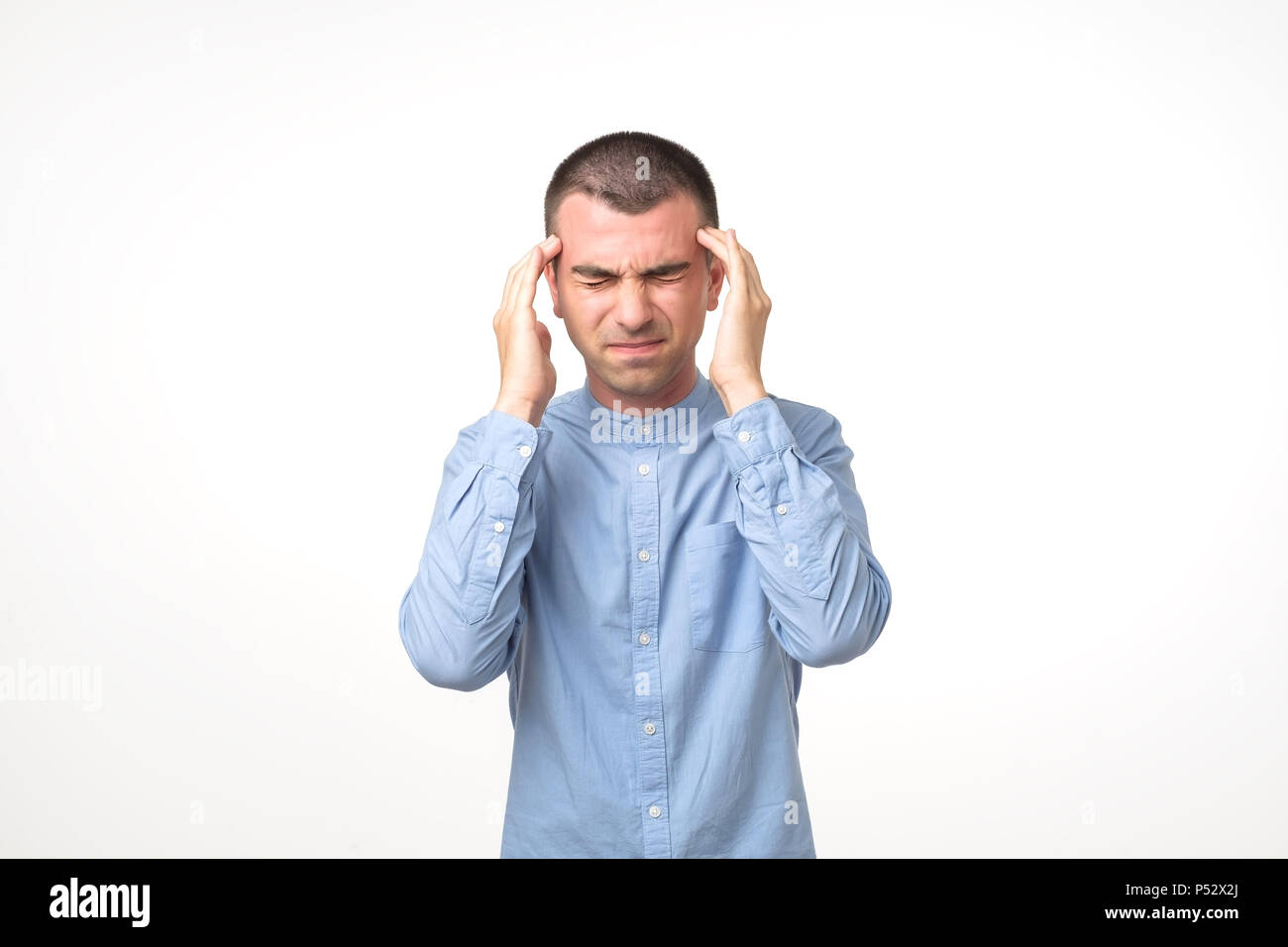 Portrait der junge Mann im blauen Hemd in Kopfschmerzen während über weißen Hintergrund stehen. Stockfoto