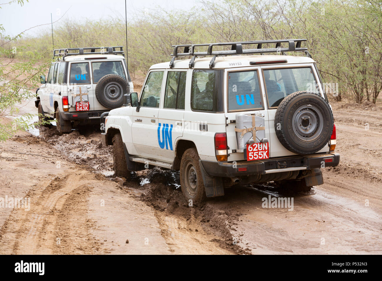 KAKUMA, Kenia - Zwei UN-Land Rover fahren auf einer verregneten Landstraße. Stockfoto