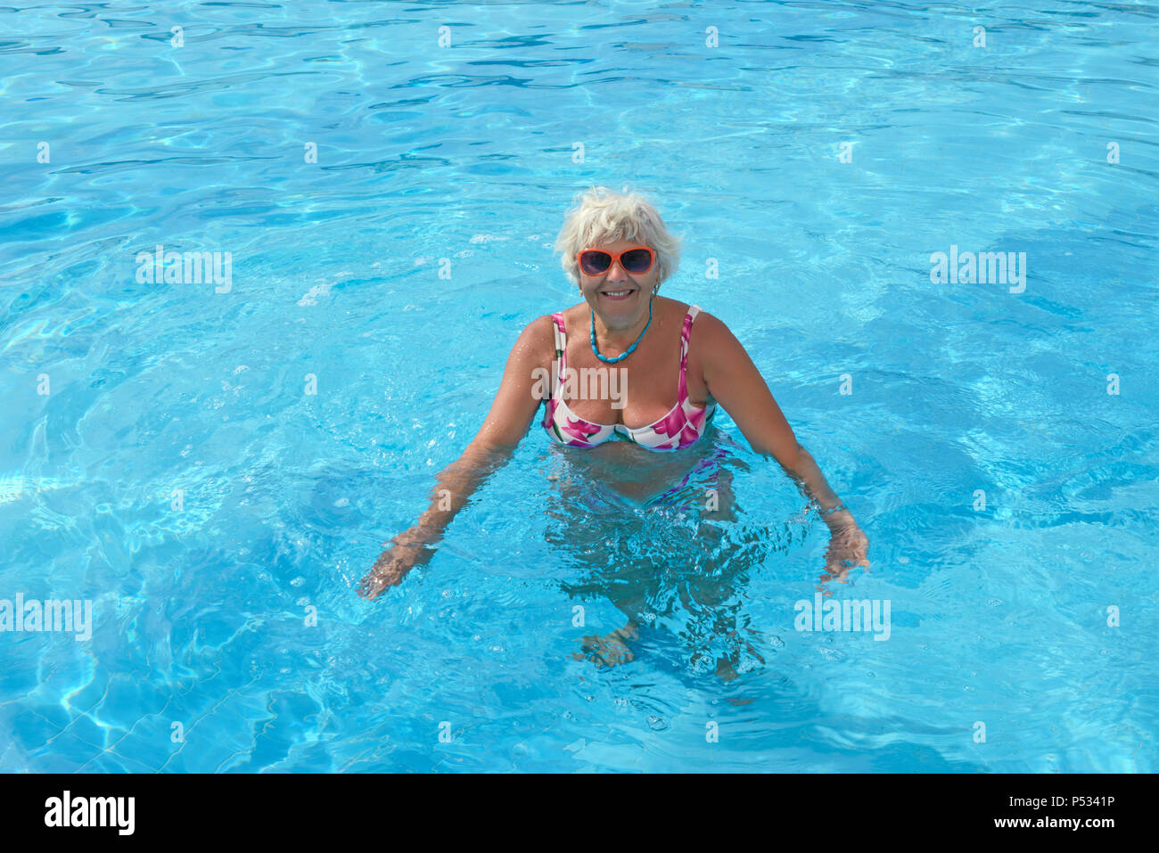 Alte Frau ist Wellness Übungen im leuchtend blauen Wasser des Pools. Stockfoto