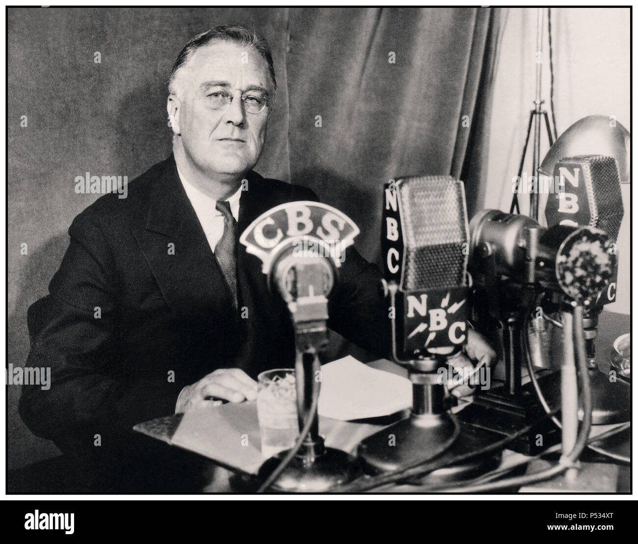 Bild des FDR Franklin D. Roosevelt aus den 1930er Jahren, der eine Radiosendung („Kamingespräch“) im September 1934 gibt. Auf seinem Schreibtisch CBS & NBC Network Broadcast Mikrofone. Franklin Delano Roosevelt Sr., oft mit seinen Initialen FDR bezeichnet, war ein amerikanischer Staatsmann und politischer Führer, der von 1933 bis zu seinem Tod im Jahr 1945 als 32. Präsident der Vereinigten Staaten diente. Stockfoto