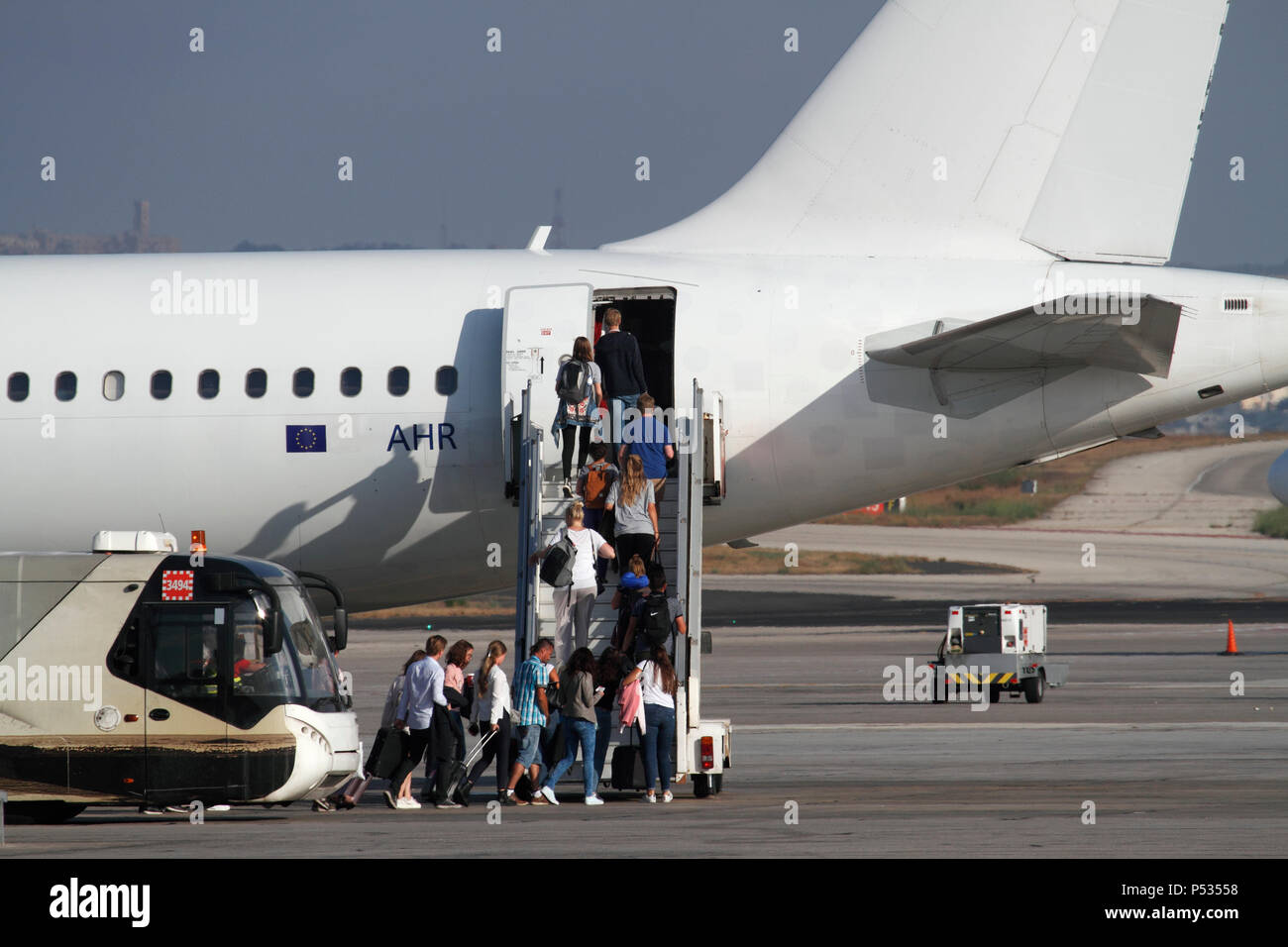 Urlaubsreisen mit dem Flugzeug. Passagiere steigen aus dem Flughafenbus und steigen in ein Düsenflugzeug über eine Rampentreppe ein. EU-Flagge auf dem hinteren Rumpf sichtbar. Stockfoto