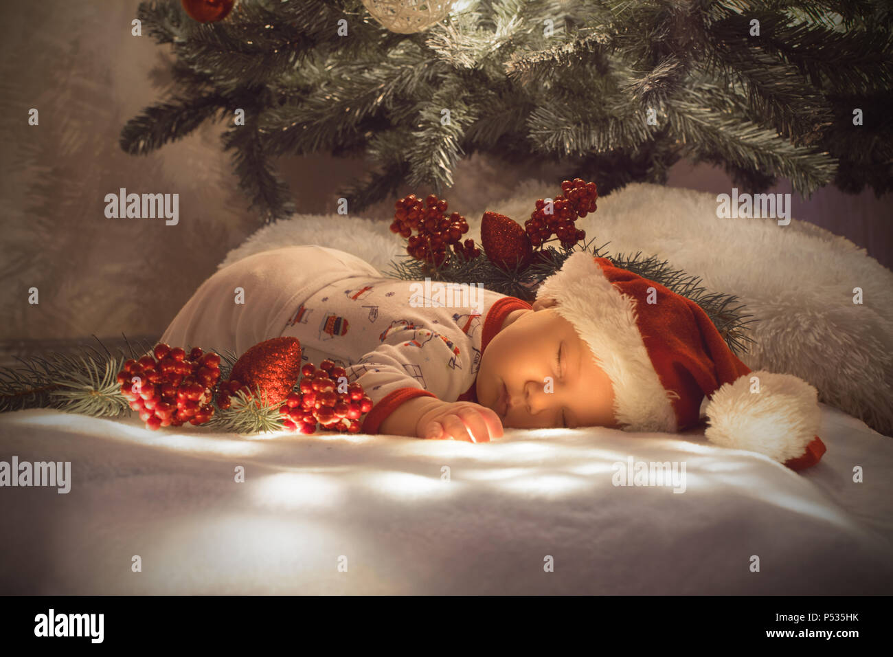 Neugeborenes Baby boy Schlafen unter Weihnachtsbaum in der Nähe viele Dekorationen. Tragen Santa's Hut Stockfoto