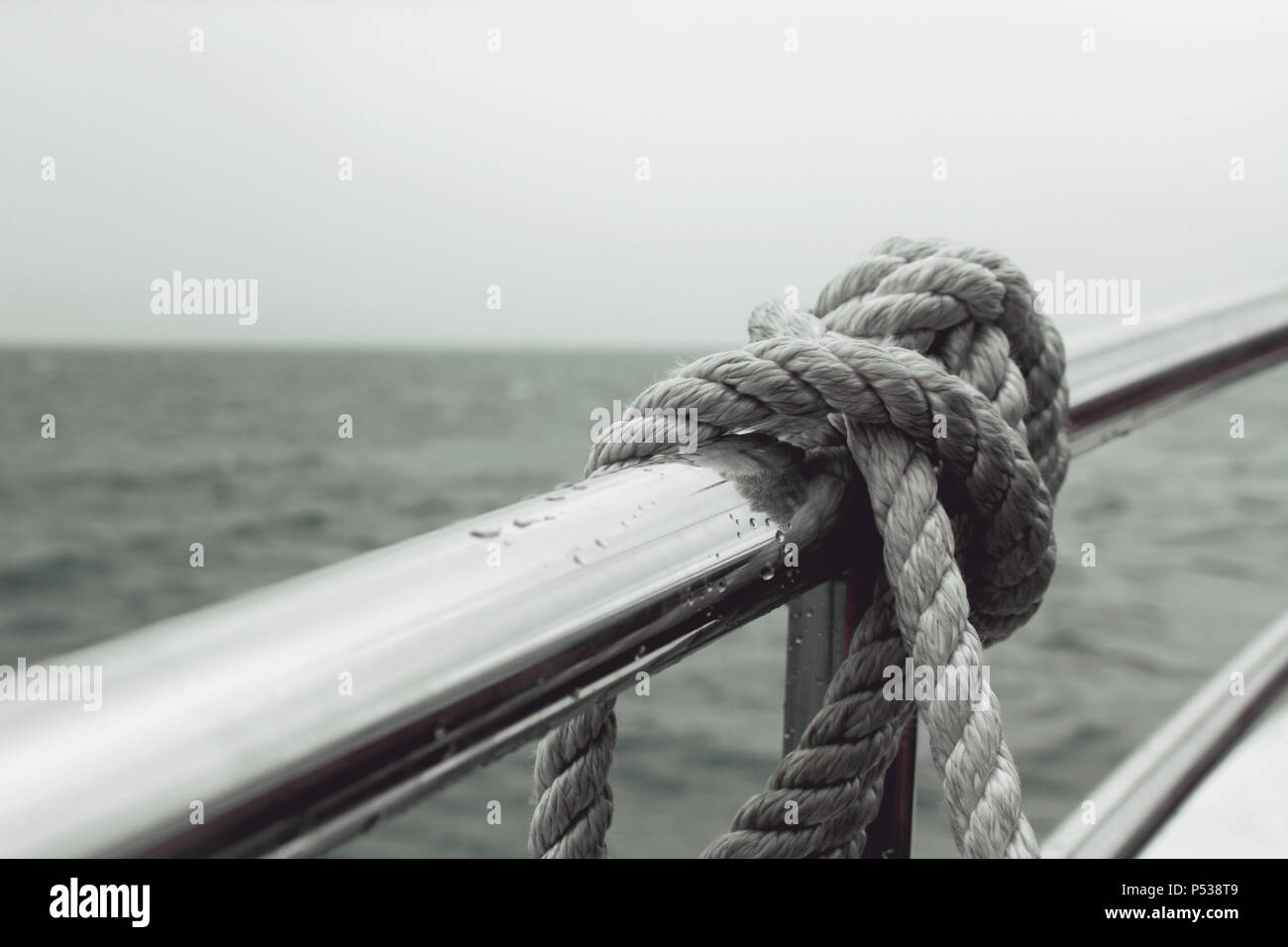 Eine Leine, die an einer Reling eines Bootes befestigt ist, das Wasser im Hintergrund, bei schlechter Sicht. Stockfoto
