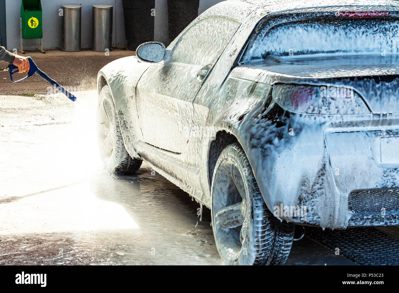 Ein mann wäscht sein auto mit schaum in einer  selbstbedienungsautowaschanlage mit rädern und reifen in der nähe