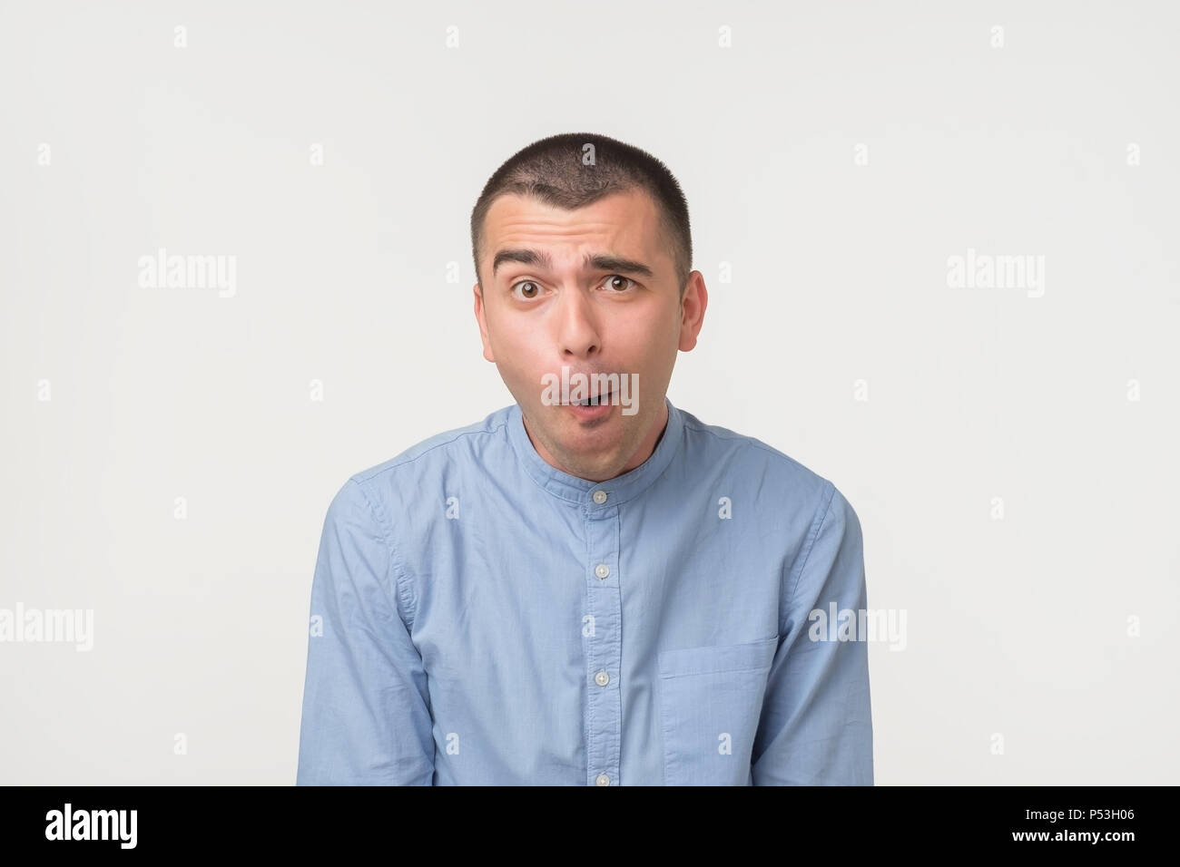 Angesicht der kaukasischen jungen Mann im blauen Hemd auf grauem Hintergrund schockiert. Er so eine wirklich hübsche Frau und verlor seine Stimme Stockfoto
