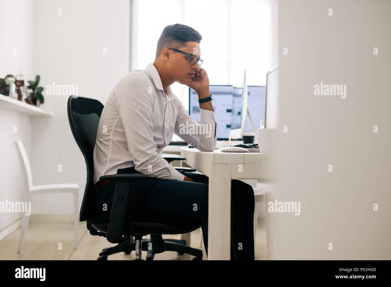 Software Entwickler sitzt in seinem Büro Schreibtisch am Computer schauen und Denken mit der Hand auf die Wange. Mann mit Brille arbeiten am Computer in o Stockfoto