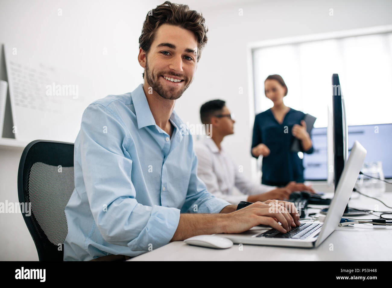 Software Entwickler im Büro sitzen, Arbeiten am Computer. Happy Anwendung Entwickler arbeitet an einem Laptop im Büro mit seinen Kollegen im Hinterg Stockfoto