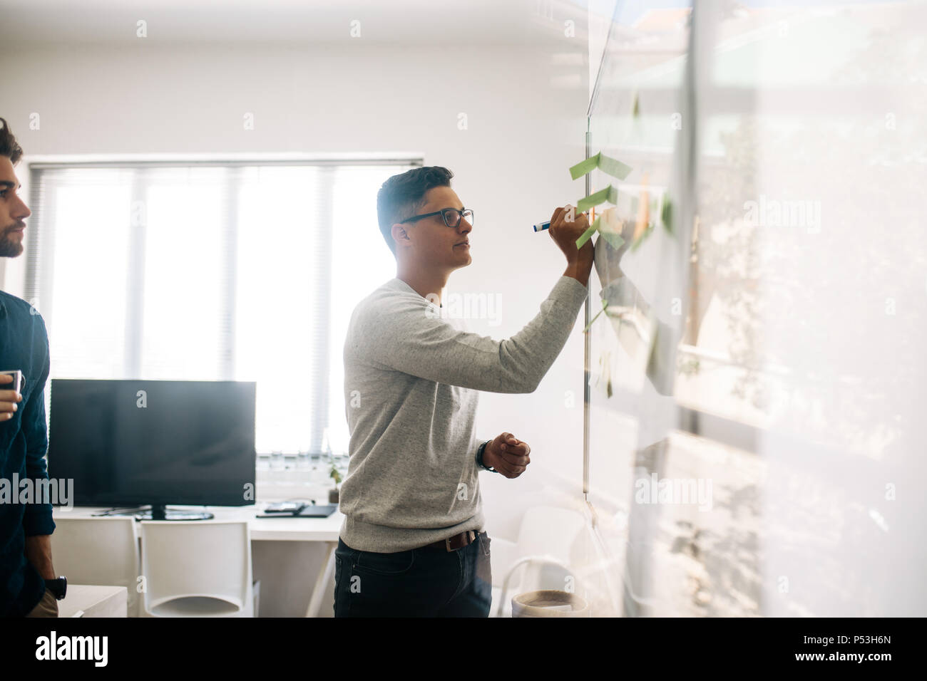 Mann schreiben an Bord im Tagungsraum, während seine Kollegen aussieht. Anwendungsentwickler im Diskutieren von Ideen und Schreiben an Bord Stockfoto