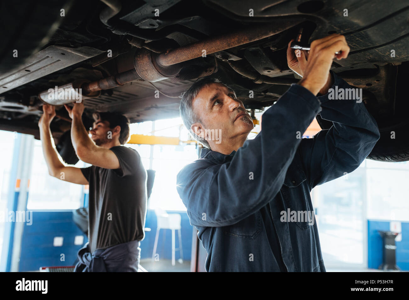 Zwei Mechaniker, der sich unter einem Auto zu schaffen. Männer in Garage reparieren Abgasanlage eines angehobenen Automobil. Stockfoto