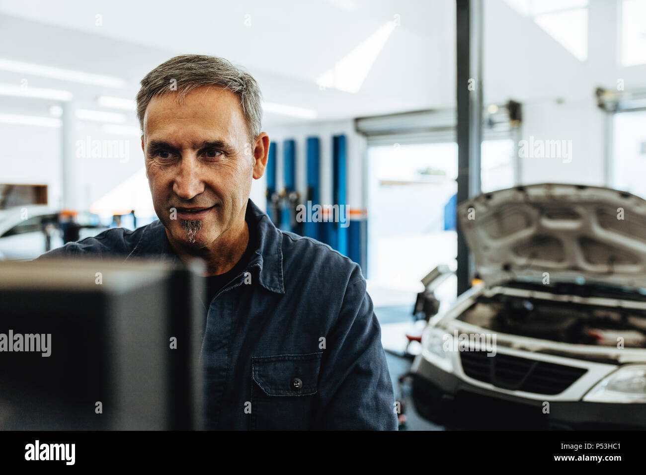 Reife männliche Mechaniker prüfen ein Auto mit Computer. Mechaniker das Auto die Diagnose auf dem Computer. Stockfoto