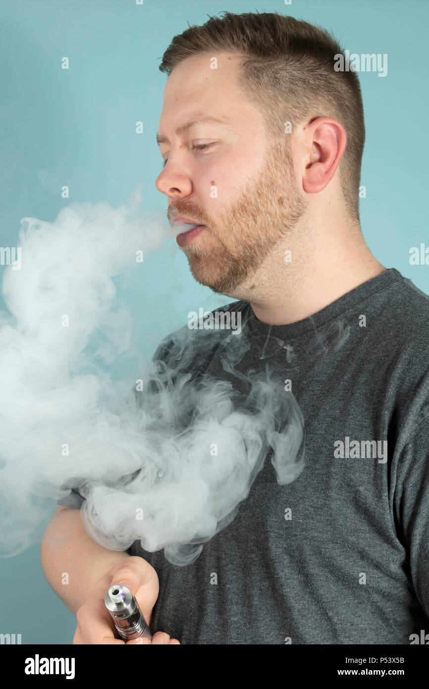Junger Mann vaping Rauchen einer Zigarette mit einer Wolke von Rauch sein  Gesicht verdeckt, als er den Verdampfer in der Hand hlt Stockfotografie -  Alamy
