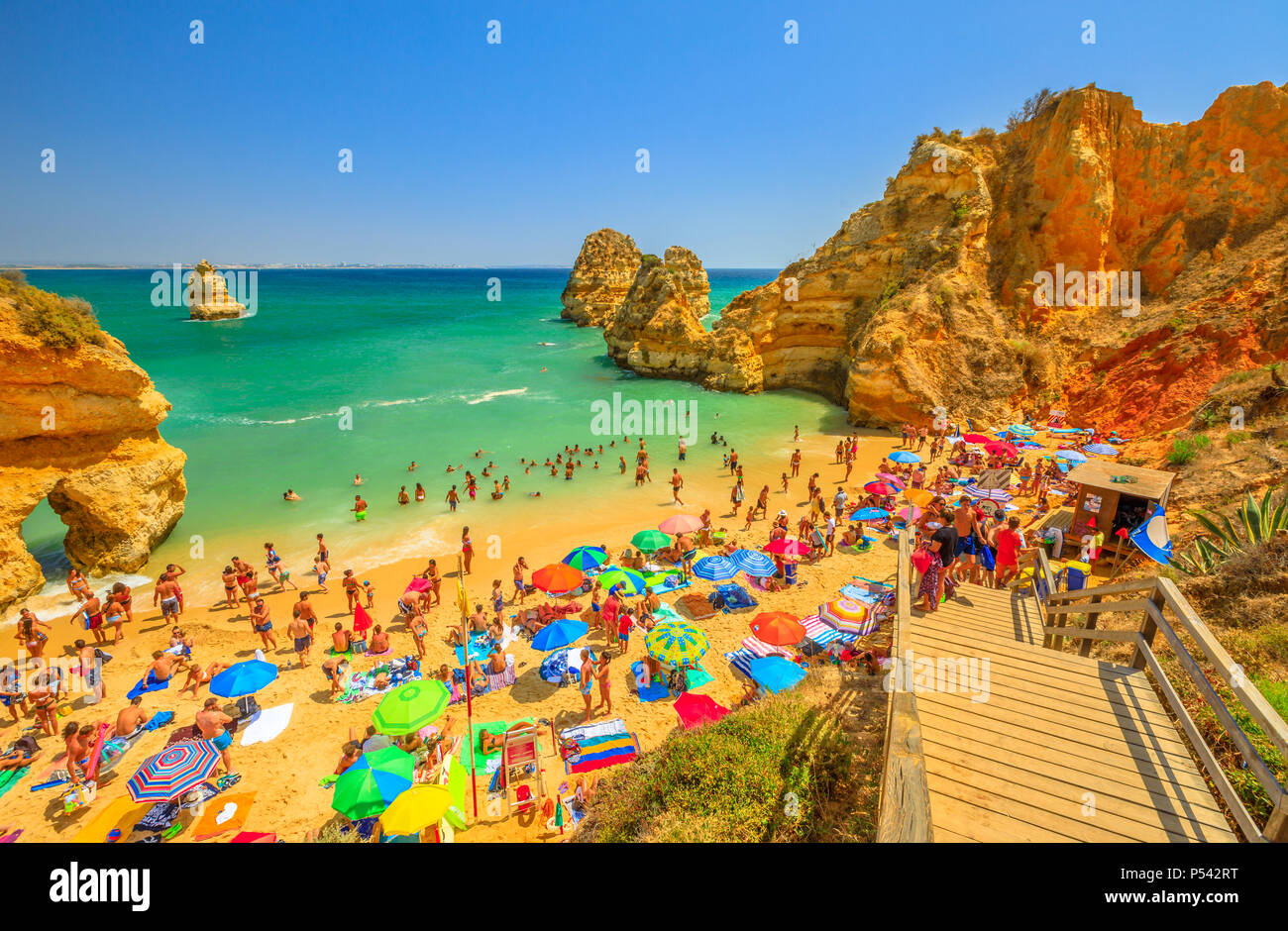 Lagos, Portugal - 21 August 2017: menschenmenge Sonnenbaden und genießen unter bunten Sonnenschirmen in beliebten Praia do Camilo in der Nähe von Ponta da Piedade. Sommer Urlaub in Algarve, Portugal, Europa Stockfoto