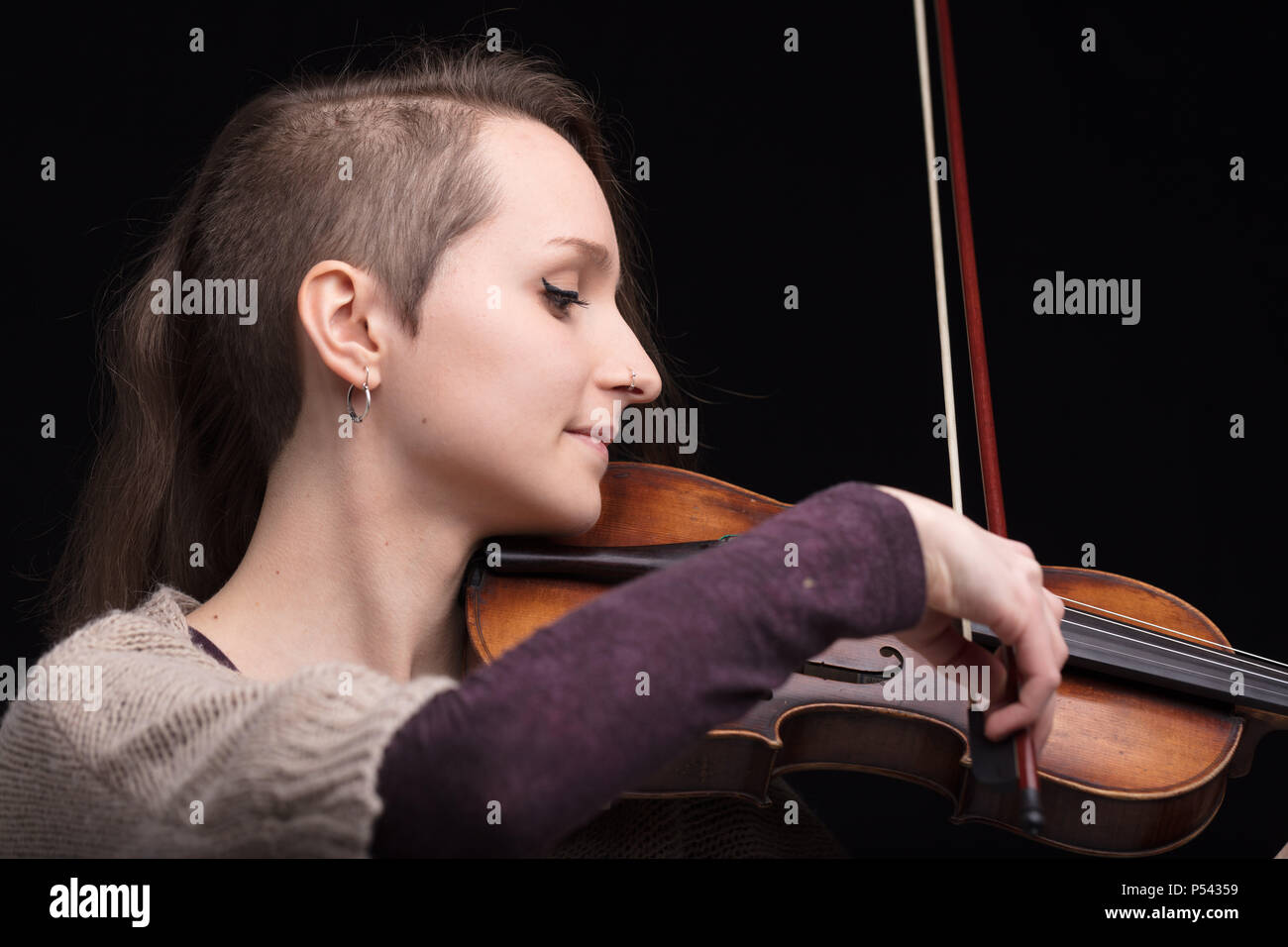 Junge Frau mit der Hälfte ihrer Haare rasiert während der Wiedergabe einer barockvioline auf schwarzem Hintergrund Stockfoto