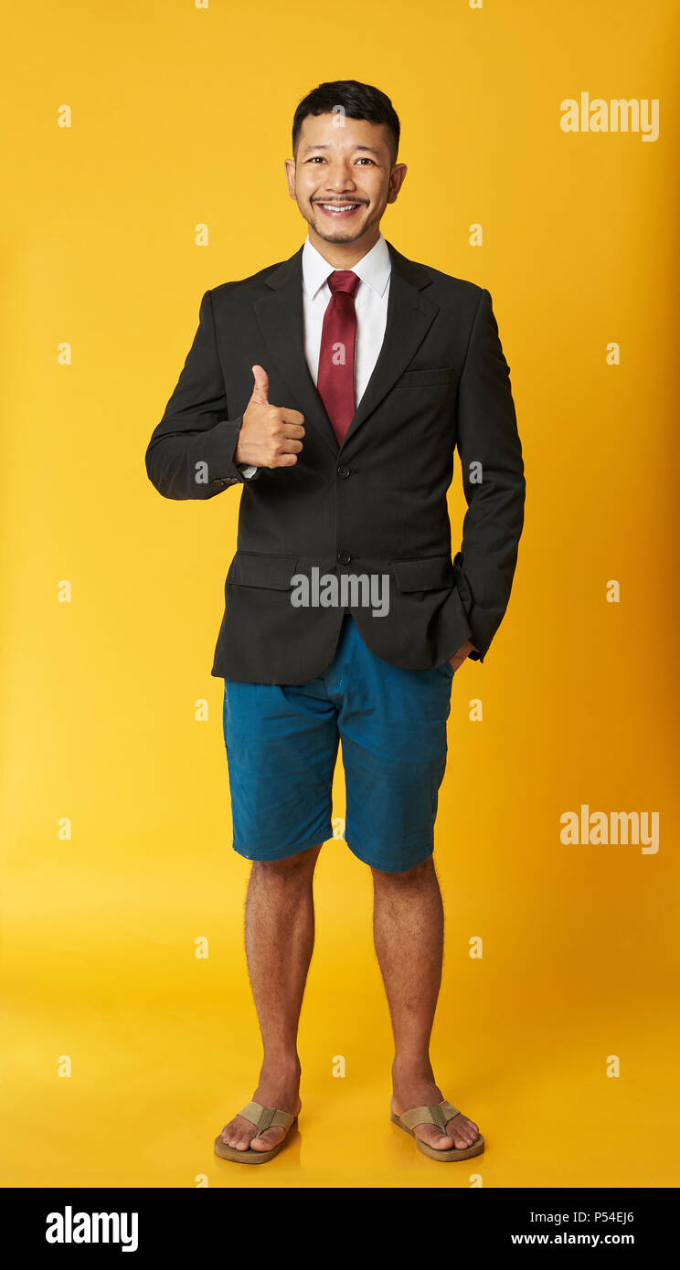 Happy asiatischer Mann in Flip Flops mit Daumen hoch auf gelbem Hintergrund Stockfoto