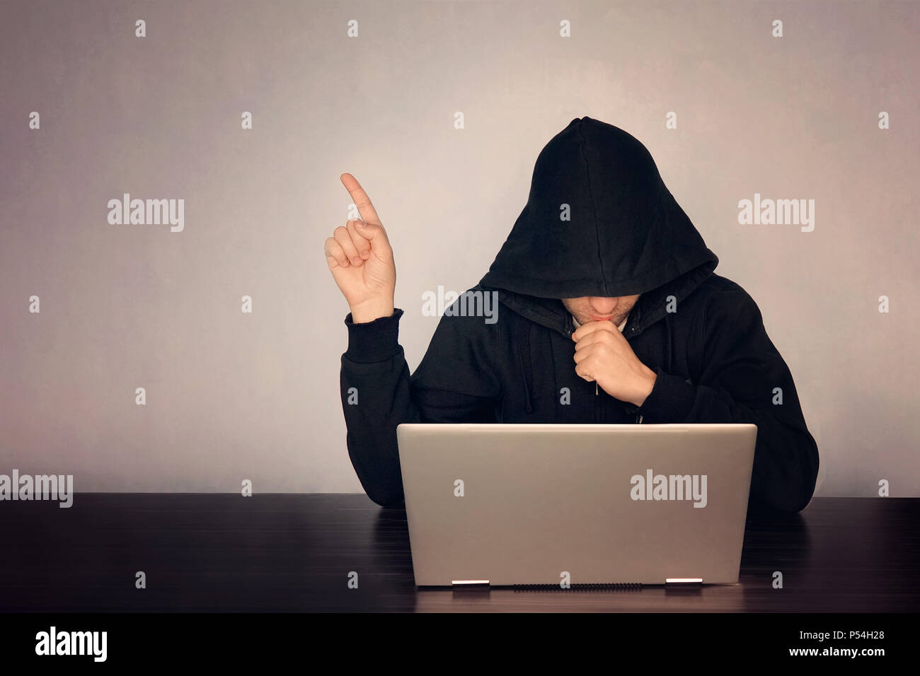 Hacker mit Kapuze vor seinem Computer zeige Finger. Dunkles Gesicht. mit Kapuze. Technologie, Konzept, Hacker punkte Finger auf leeren Raum für Text Stockfoto