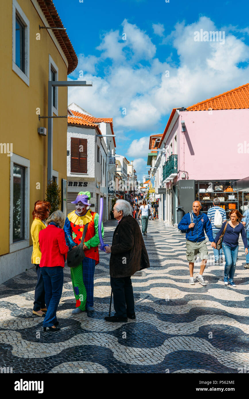 Ein Mann verkleidet als Clown zu den Einheimischen auf einer belebten Einkaufsstraße im Herzen von Cascais, Portugal spricht Stockfoto