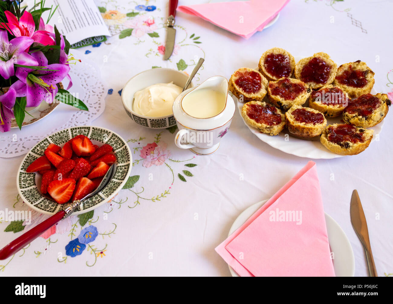 Cream Tea mit Scones, Erdbeeren und Erdbeermarmelade heraus auf eine bunte Tischdecke gelegt. Stockfoto