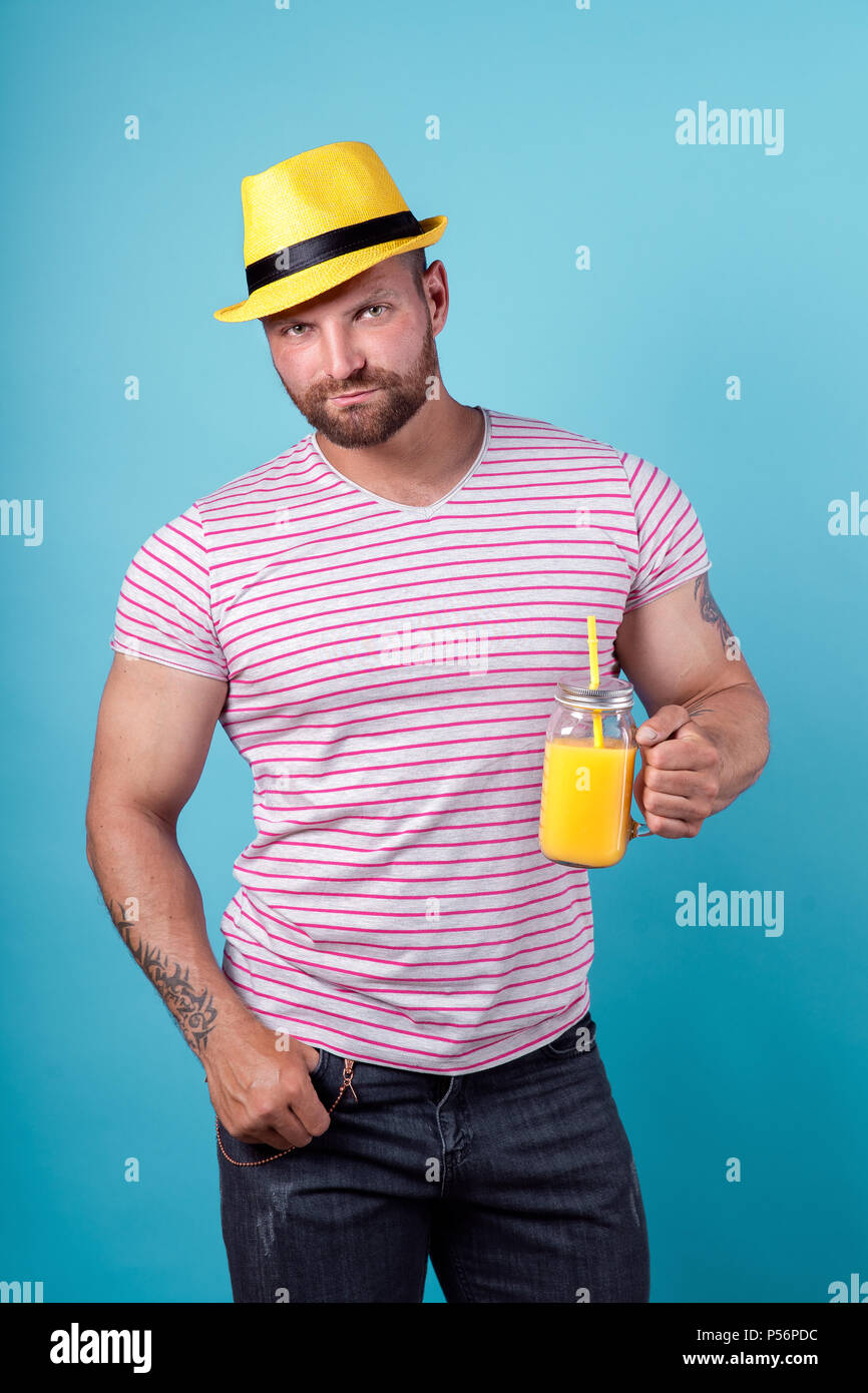 Kreative männlichen im Sommer gestreiftes Hemd mit Cocktail Flasche entspannt und Stroh Hut gelb auf blau studio Hintergrund Stockfoto