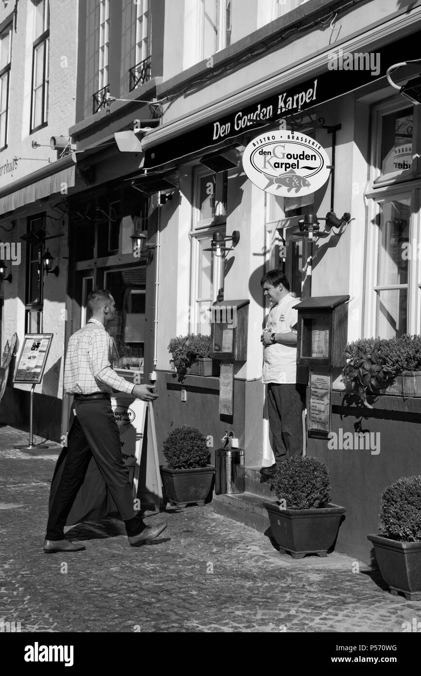Huidenvettersplein, Brugge, Belgien: Chef steht in der Tür von den Gouden Karpel Restaurant, im Gespräch mit dem Kellner. Schwarz und Weiss Stockfoto