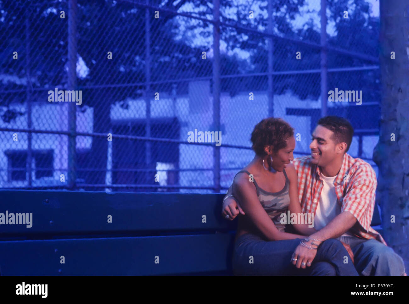 Junge, Urbane, ethnischen Paar auf einer Parkbank in der Abenddämmerung oder am frühen Abend flirten Stockfoto