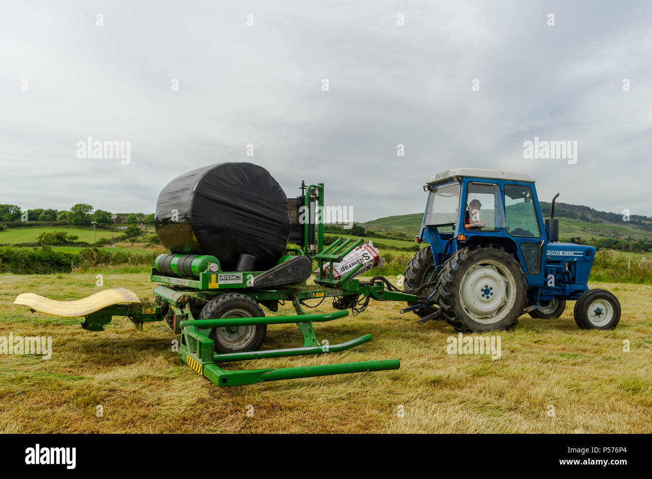 Ballydehob, West Cork, Irland. 25. Juni 2018. Alan Pyburn von Hollum John O'Driscoll Silage Auftragnehmern auf der Grundlage wickelt eine silage Kaution auf das ballydehob Bauernhof von Ben Deane auf einem sehr warmen Tag. Dies ist der Auftakt zu einer Mini-Hitzewelle, in der Temperaturen gesetzt sind, zu erreichen 31°Grad Celsius bis Donnerstag dieser Woche. Credit: Andy Gibson/Alamy Leben Nachrichten. Stockfoto