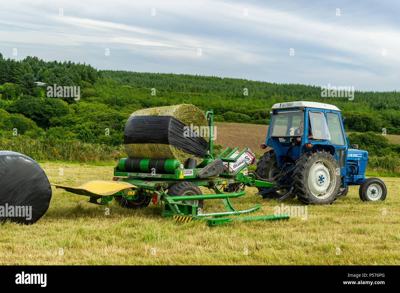 Ballydehob, West Cork, Irland. 25. Juni 2018. Alan Pyburn von Hollum John O'Driscoll Silage Auftragnehmern auf der Grundlage wickelt eine silage Kaution auf das ballydehob Bauernhof von Ben Deane auf einem sehr warmen Tag. Dies ist der Auftakt zu einer Mini-Hitzewelle, in der Temperaturen gesetzt sind, zu erreichen 31°Grad Celsius bis Donnerstag dieser Woche. Credit: Andy Gibson/Alamy Leben Nachrichten. Stockfoto