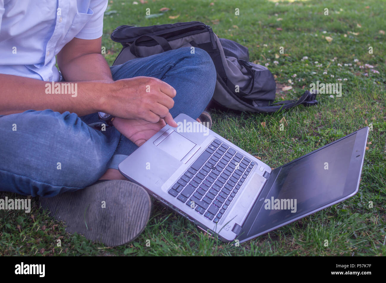 Eine Person mit seinem Laptop und dabei einige Arbeit in einer Wiese oder Garten. Stockfoto