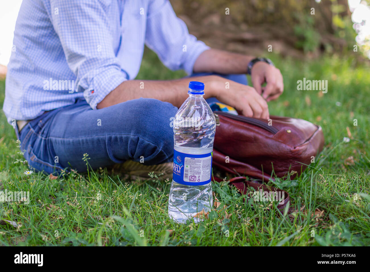 Srinagar, Jammu und Kaschmir, Indien: vom: 1. Juni 2018 - eine Person in einer Wiese oder einen Garten Holding seine Tasche in seinen Händen sitzen und eine Flasche Wasser Stockfoto
