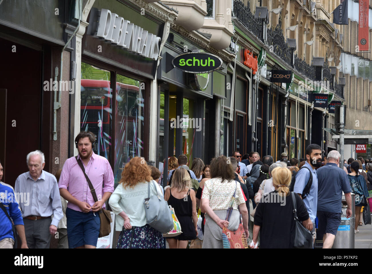 Käufer und Touristen zu Fuß entlang Magdalen Street, Oxford, wo High Street Einzelhändler wie Supermärkte Sainsbury's Lokale, Tesco Metro, der Schuh r Stockfoto