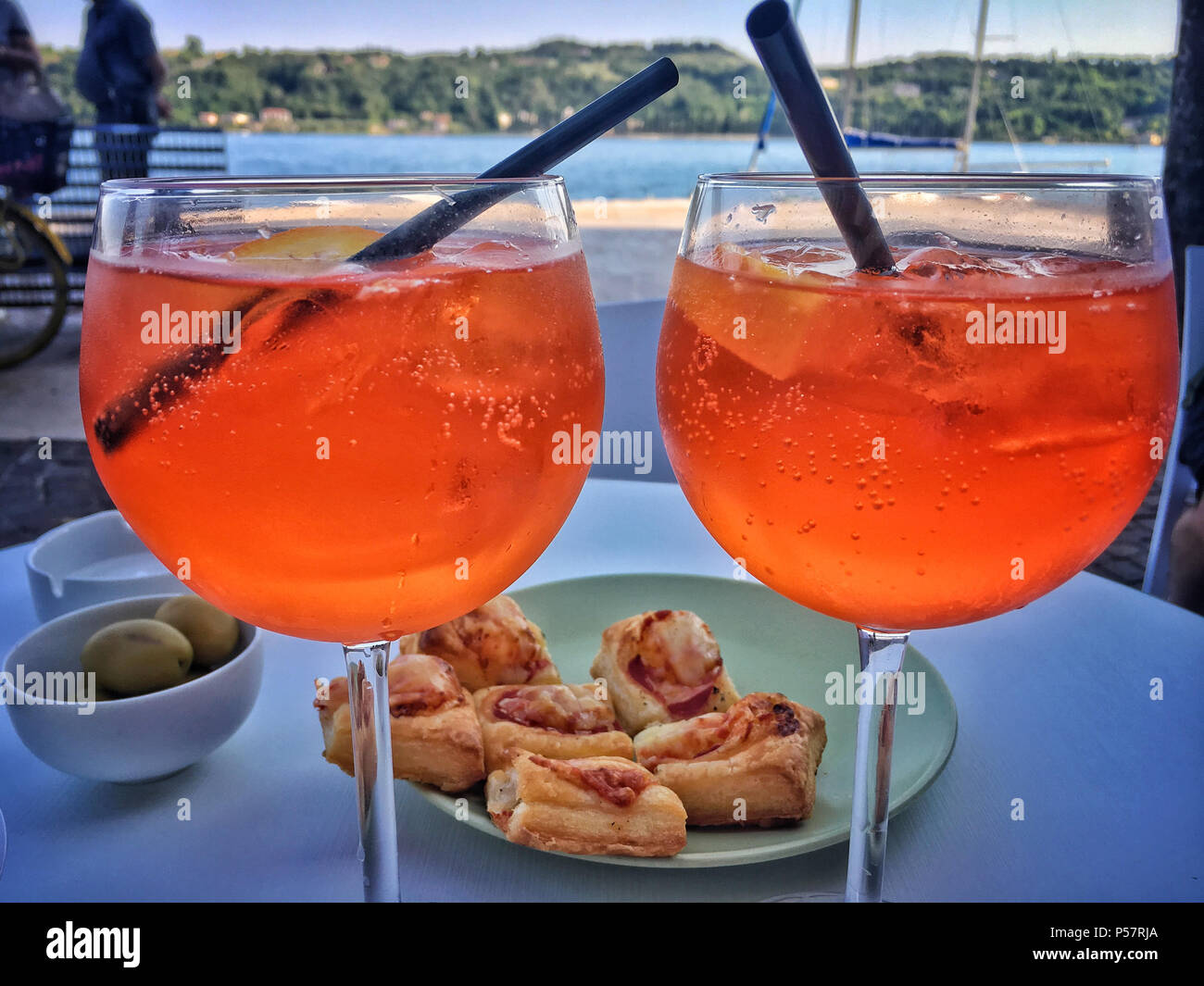 Zwei Gläser Aperol Spritz trinken mit ein paar Snacks auf einem Tisch vor  dem Gardasee Stockfotografie - Alamy