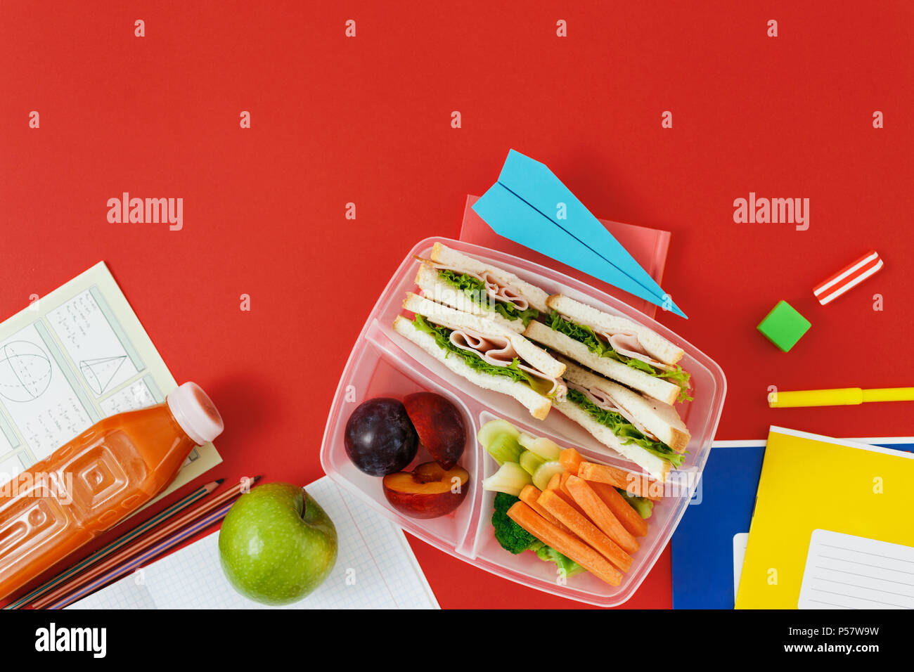 Gesunde Schule Lunch Box mit Sandwich, Gemüse, Saft und Obst auf rotem Hintergrund mit Kopie Raum, Ansicht von oben. Gesunde Ernährung Konzept. Flach compo Stockfoto