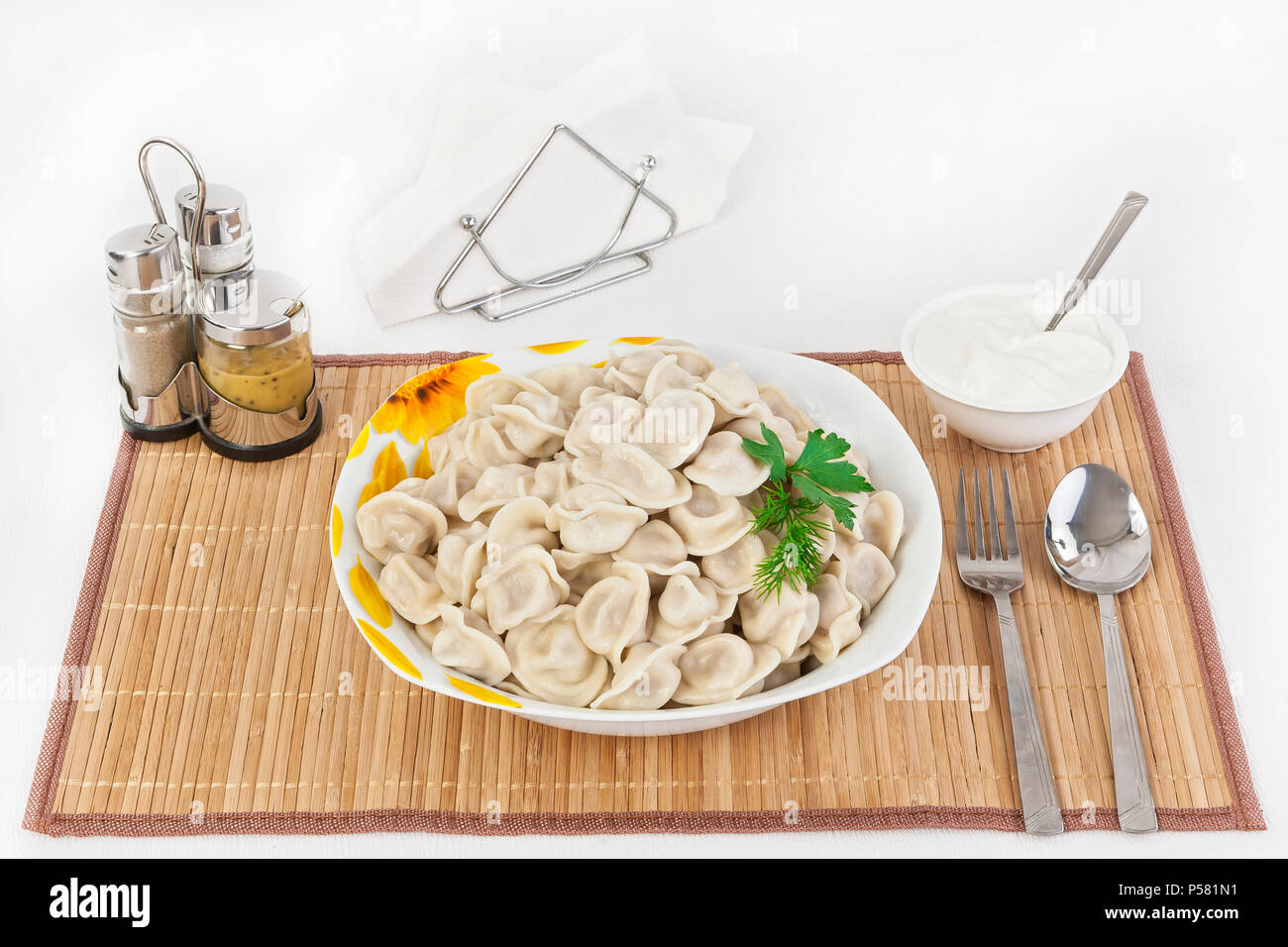 Russische Knödel mit Kräutern und Zwiebeln. Ravioli mit Fleisch. Das Gericht ist in einem Teller serviert. Serviert mit Knödel ist Sauerrahm in eine Schüssel geben. Stockfoto