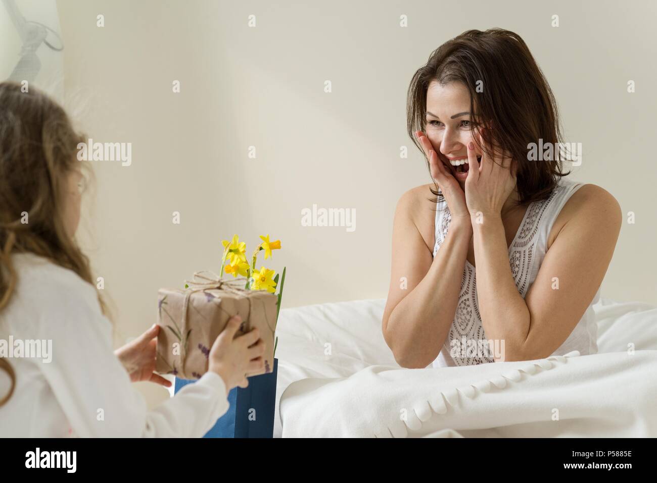 Muttertag. Die kleine Tochter hält ein Geschenk und Blumen für Ihre Mutter. Hintergrund Interieur der Zimmer, der Mutter im Bett, morgen Stockfoto