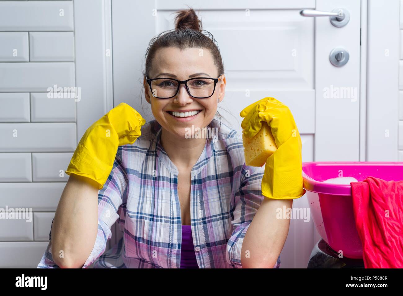 Professionelle Reinigung. Frau Hausmädchen in gelbe Gummihandschuhe mit Detergenzien lächelnd gegen weisse Türen Stockfoto