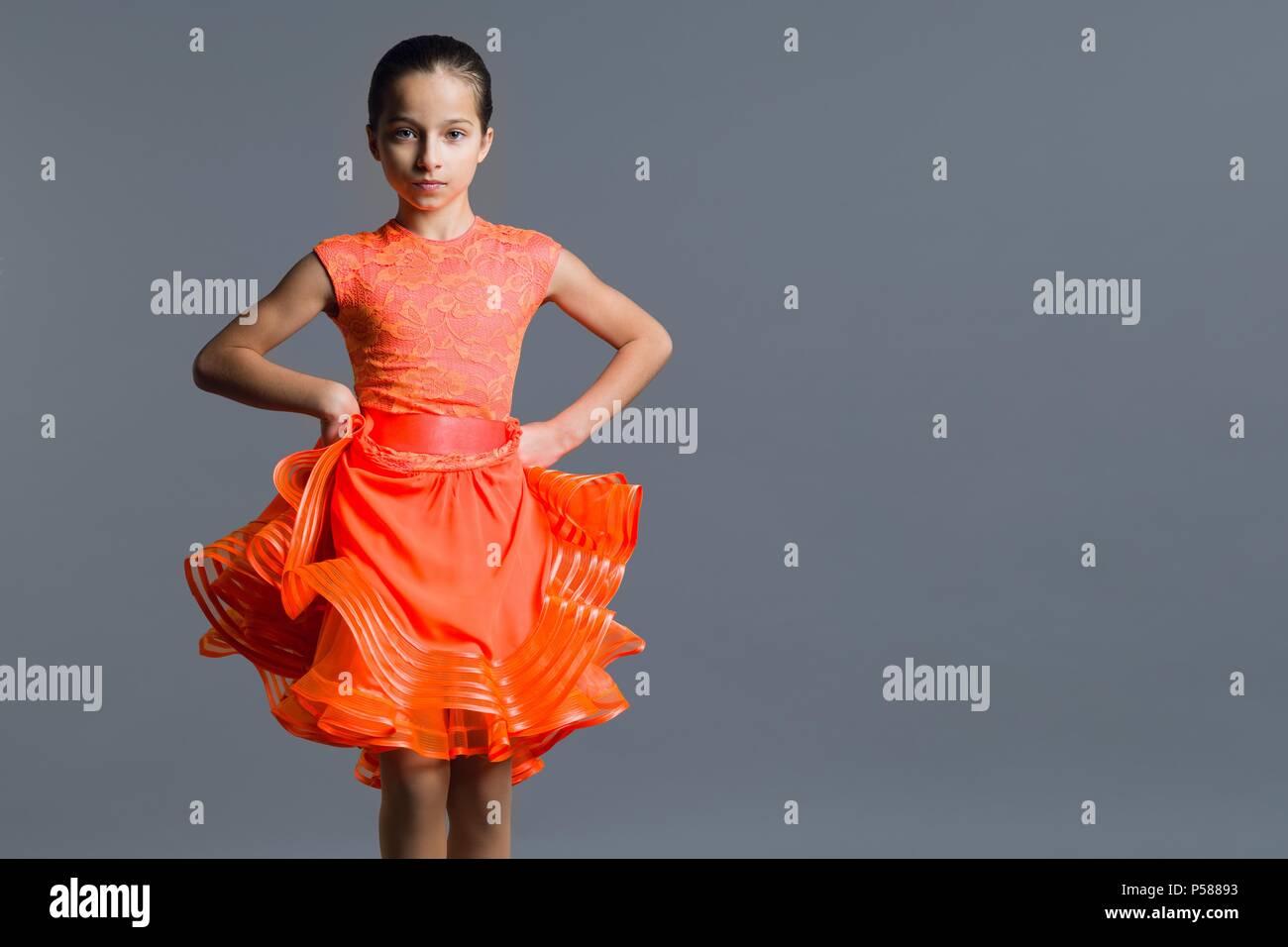 Porträt eines Mädchens, das Kind 9-10 Jahre Tänzer. Sport Gesellschaftstänze, Latino. Mädchen in einem orangefarbenen Kleid auf einem grauen Studiohintergrund, kopieren Raum Stockfoto