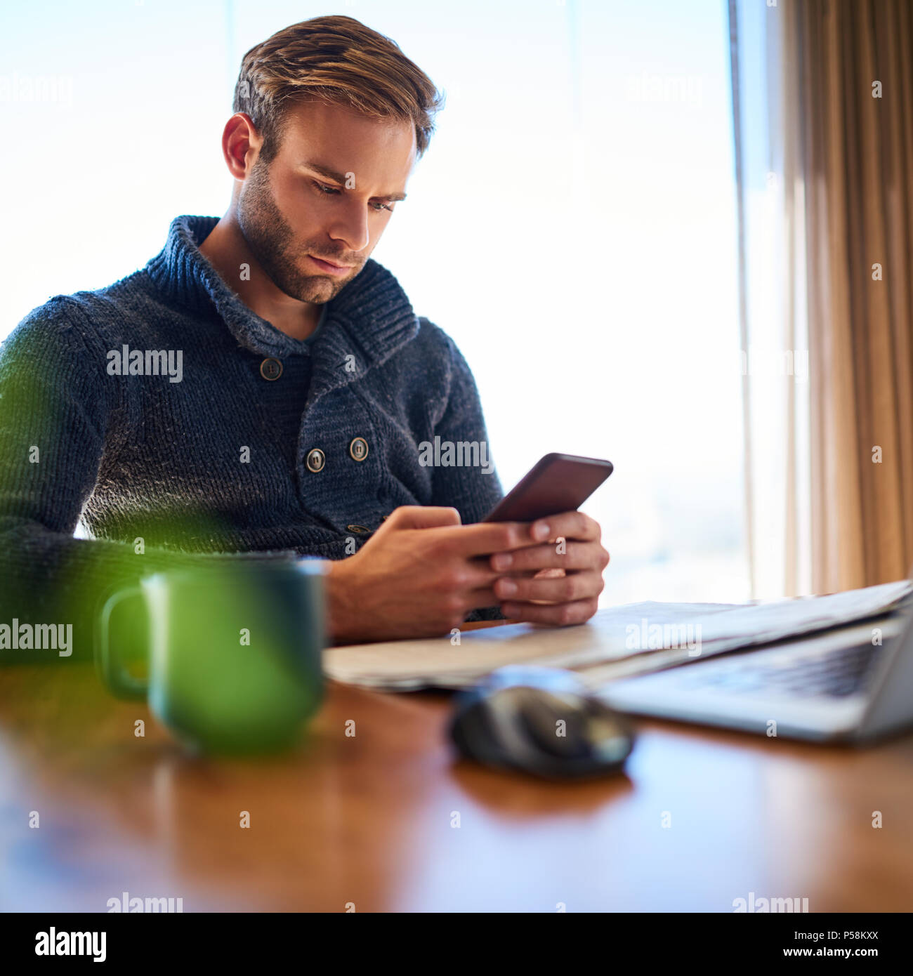 Platz Bild von gutaussehenden jungen weißen Mann besetzt Sms auf seinem Mobiltelefon während an seinem Schreibtisch bei der Arbeit sitzen, procrastinating anstatt zu arbeiten. Stockfoto